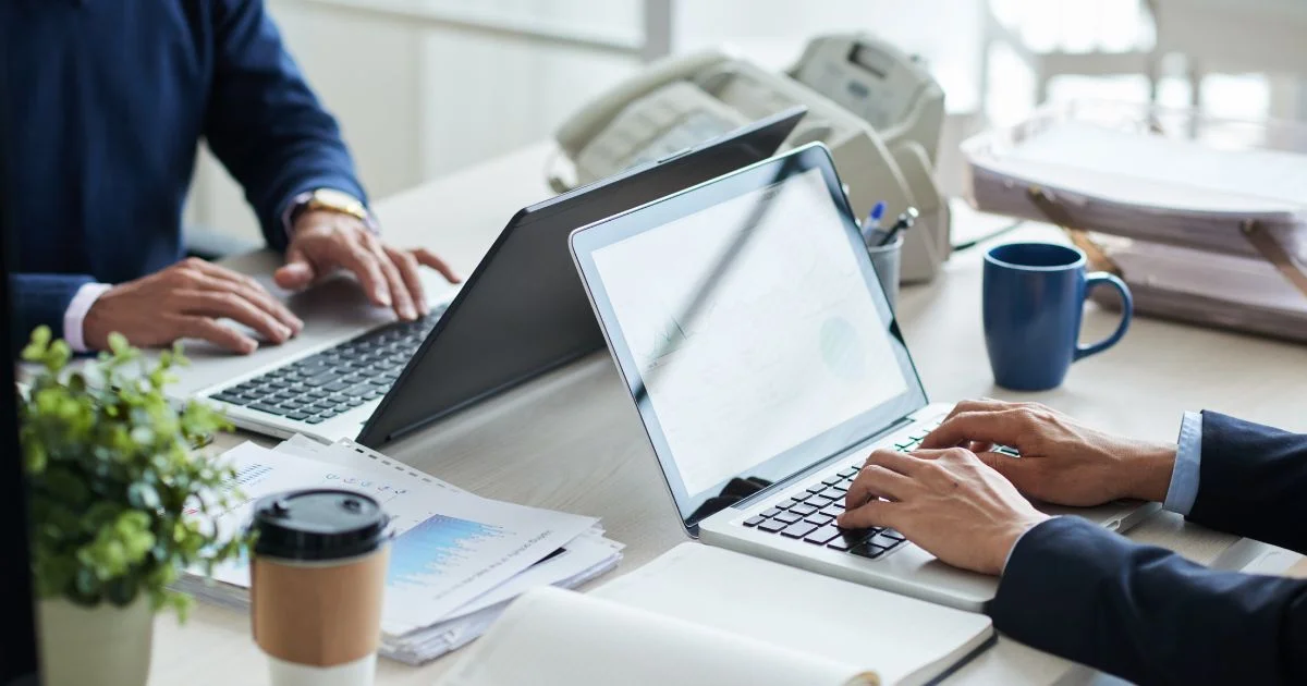 Business professionals working together at shared office desk with laptops