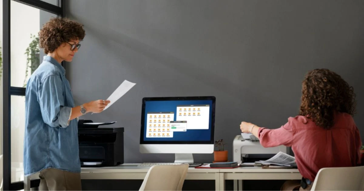 Two women printing and reviewing documents at modern office desk
